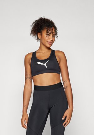 Sujetador deportivo atlético negro hecho de material suave con un logo blanco de Puma. Combinado con leggings negros de cintura alta, que destacan un diseño ajustado.