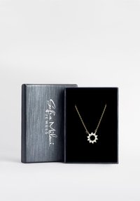Guldkæde med vedhæng i blomstermotiv med hvide ædelstene, præsenteret i en mørkeblå, struktureret gaveæske med et sølvfarvet logo.