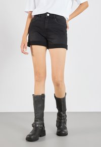 Black denim shorts with a fitted design and rolled hems, paired with tall black leather boots featuring buckle and stud detailing.