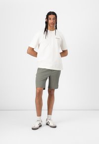 Hvid bomulds T-shirt med logo, parret med grønne teksturerede shorts. Accessories inkluderer hvide sneakers med grå detaljer og hvide sokker.