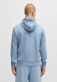 Ljusblå hoodie gjord av mjukt tyg. Har dragsko i huvan, ribbade muddar och nederkant. Baksidan är plain utan några grafik eller mönster.
