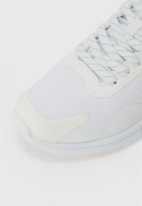 Baskets blanches à tige en maille, avec des superpositions lisses et une semelle texturée. Les lacets sont gris clair avec un motif subtil.