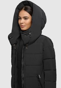 Fekete puffermek látható, nagy, strukturált kapucnival, cipzáras elejével és oldalsó zsebeivel. Tömörített mintázattal és patent gombokkal rendelkezik.