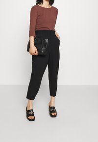 Brązowy długi rękaw bluzka, czarne spodnie z wysokim stanem wąskie, czarna kopertówka i czarne sandały na słupku. Gładkie tekstury i prosty design.