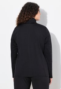 Svart atletisk jacka med slät tyg, slim fit, hög krage och mönstrade ärmar med struktur, samt ytterligare reflektoriska detaljer.