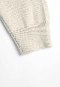 Manica di maglione a maglia color beige chiaro con polsino a costine. Tessuto liscio, morbido e finitura pulita all'orlo. Nessun motivo o accento visibile.