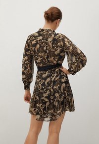 Robe noire à motifs cachemire en tissu transparent, avec manches longues, ourlet volanté et taille noire cintrée.