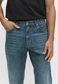 Denimjeans i medelblå tvätt, med rak passform, fem fickor och en klassisk knappgylf. Diskret blekning och sydda detaljer.