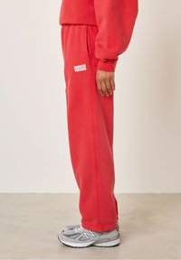 Punased puuvillased dressipüksid elastse vöökoha ja küljetaskutega, millel on valge "AMERICAN VINTAGE" logo. Kombineeritud hallide sportlike kingadega.