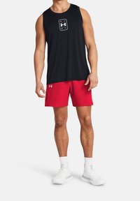 Camiseta deportiva sin mangas negra con un logo blanco, combinada con pantalones cortos rojos y zapatillas blancas. Tejido suave y ligero.