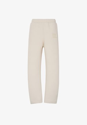 Pantalons de survêtement beiges avec une taille élastiquée, arborant un logo en relief subtil sur la cuisse supérieure. Fabriqués en tissu doux et texturé.