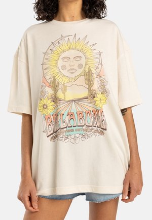 Krémové oversized tričko s grafickým designem zobrazujícím slunce, kaktusy, květiny a text "BILLABONG" v pestrých vzorech. Jemná textura.