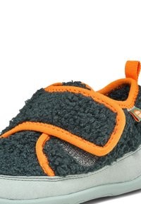 Pantofole verdi pelose con accenti arancioni e strap in Velcro. Presentano una parte superiore testurizzata, un pannello laterale grigio e una suola grigio chiaro.