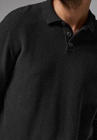 Schwarzer Poloshirt-Pullover aus strukturiertem Strickstoff, mit einem Kragen und einer Knopfleiste mit zwei Knöpfen. Weiches und lässiges Design.