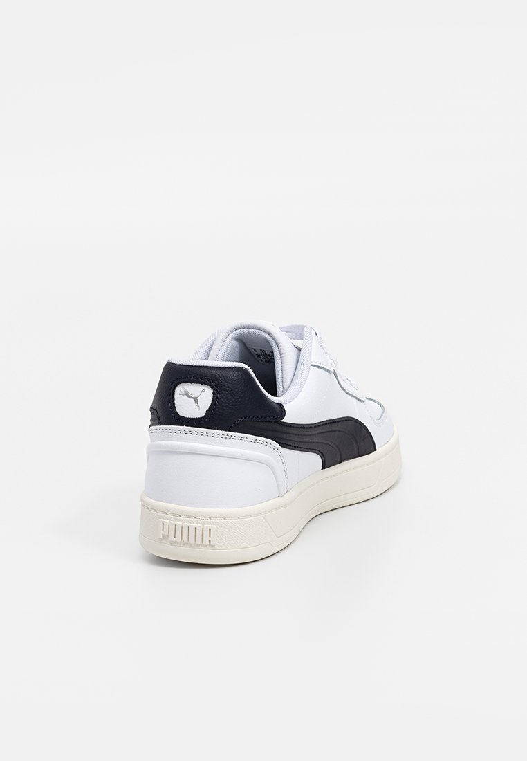 Białe i czarne sneakersy Puma widziane z tyłu, pokazujące piętę z logo Puma i kremową podeszwą na białym tle.