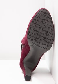Chaussure à talon haut en daim bordeaux avec fermeture éclair et semelle en caoutchouc noire texturée, avec le détail embossé "Tamaris".