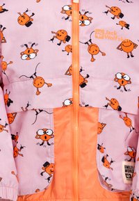 Giacca rosa con volti di cartone animato arancioni, chiusura con zip e una sezione inferiore arancione a contrasto. Il materiale sembra leggero e ha una consistenza liscia.