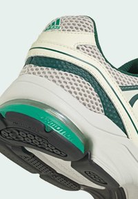 Sneaker with a gray mesh upper, green accents, and a white sole. Features a visible air unit and textured patterns on the sole.