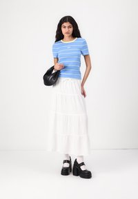 Top de manga corta a rayas azul y blanca con toques amarillos, falda maxi blanca en capas, bolso negro, calcetas blancas y zapatos de plataforma negros.