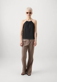 Top negru cu decolteu halter dintr-un material ușor, asortat cu pantaloni bej croiți, cu croială lejeră și textură netedă; modelul poartă ochelari de soare.