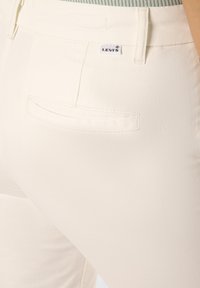 Levi's white jeans featuring a back pocket, smooth texture, and minimalistic design with a visible tag showing the brand name.