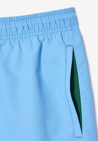 Jasnoniebieskie szorty z elastycznym paskiem, gładką teksturą i zieloną wewnętrzną kieszenią po prawej stronie.