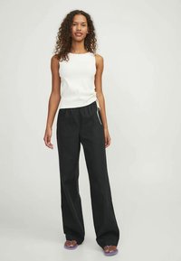 Un top alb fără mâneci, asortat cu pantaloni negri evazați, cu talie elastică și buzunare laterale. Material moale cu o croială lejeră.
