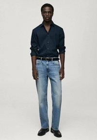Donkerblauwe lange mouwen shirt, lichtblauwe rechte jeans, zwarte riem en zwarte schoenen. Eenvoudig ontwerp zonder patronen of accenten.