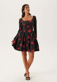 Abito nero con maniche lunghe, caratterizzato da motivi di rose rosse, scollatura quadrata, corsetto aderente e gonna a ruota. Tessuto di consistenza liscia.