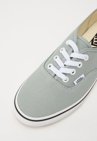 Vans sneakers i ljusgrön canvas med vita snören, som har en texturerad ovansida, svart kant och logotypdetalj på sidan.