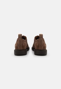 Scarpe in suede marrone con dettagli brogue, punta rotonda e suole in gomma nera a contrasto. Presentano linguette sul tallone per una facile calzata.