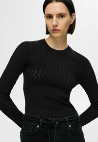 Zwarte longsleeve trui met gestructureerde diamantpatronen en geribbelde ronde hals, gecombineerd met hooggesneden donkere jeans.