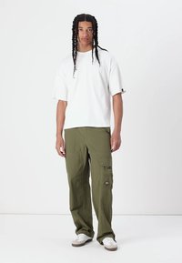 T-shirt blanc à manches courtes et coupe décontractée associé à un pantalon cargo vert olive avec une poche plaquée et un tissu texturé.