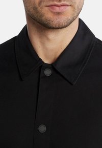 Camicia nera con bottoni, caratterizzata da un colletto classico, una texture di tessuto liscia e un accento logo discreto sul bottone.