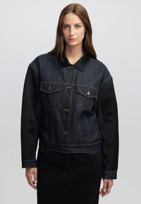 Giacca in denim e finta pelle con un lavaggio scuro, chiusura a bottoni, tasche sul petto e maniche nere a contrasto. Design con colletto classico.