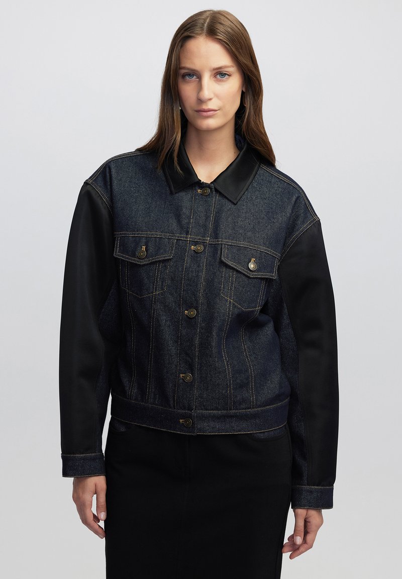 Giacca in denim e finta pelle con un lavaggio scuro, chiusura a bottoni, tasche sul petto e maniche nere a contrasto. Design con colletto classico.