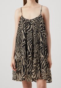 Vestido de estampado animal con un ajuste holgado, tirantes delgados y volantes en capas. La tela es ligera con un patrón de cebra en negro y beige.