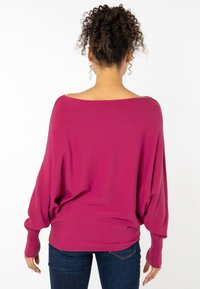 Lässiger, schulterfreier Pullover in leuchtendem Magenta, aus weichem Stoff mit langen Ärmeln und gerippten Bündchen, in einer lässigen Silhouette gestaltet.