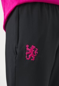 Schwarze Hose mit einem rosa gestickten Löwenlogo auf der linken Seite, mit glattem Material und lässigem Design. Der Bund ist gerafft.