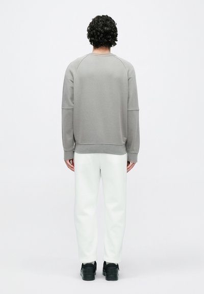 Sweatshirt cinzento com decote redondo, mangas raglã e bainha canelada, combinado com calças brancas afuniladas e ténis pretos.