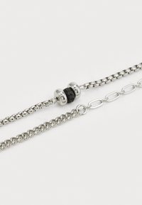 Silver chain bracelet featuring a central black bead with metallic accents, textured links, and a combination of flat and round links.