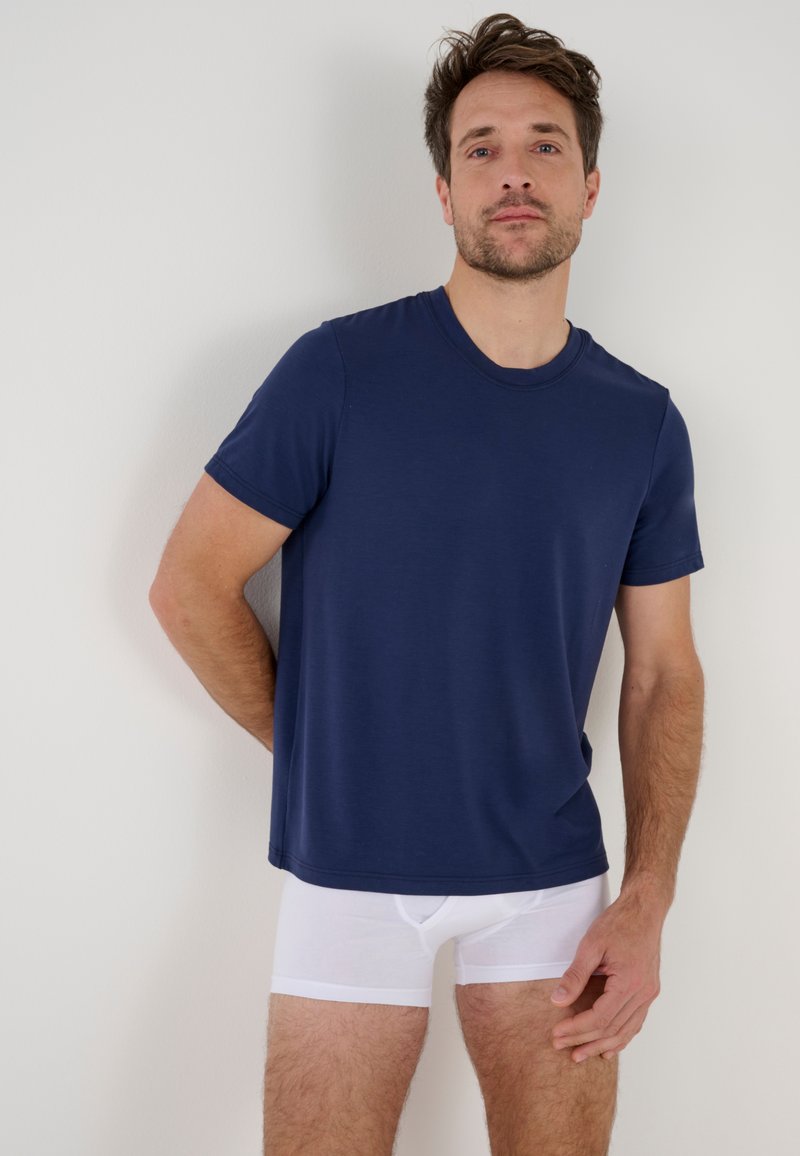 T-shirt a maniche corte blu navy in tessuto liscio, colletto a giro, abbinato a boxer bianchi aderenti. Design semplice e moderno, senza stampe.