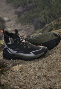 Μαύρα και γκρι πεζοπορικά παπούτσια Adidas Terrex σε βραχώδες έδαφος, που δείχνουν ανθεκτική σόλα με πέλμα από καουτσούκ Continental.