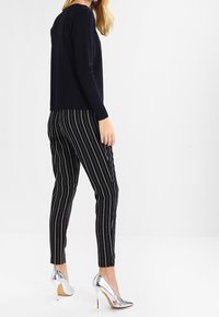 Schwarz-weiß gestreifte Hose, slim fit, kombiniert mit einem marineblauen Pullover und glänzenden silbernen High Heels. Glatter Stoff und maßgeschneiderte Passform.