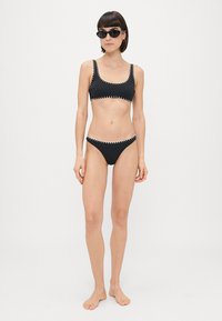 Juodas bikininis komplektas su stačiakampiu viršumi ir žemais šortukais, puoštais kontrastingomis siūlėmis palei kraštus.