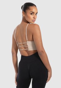 Beige geribbeld bralette met dunne bandjes en een gekruist rugontwerp, gecombineerd met hooghoge zwarte leggings. Gladde textuur, lichtgewicht stof.