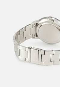 Montre en acier inoxydable argentée avec un bracelet poli, présentant des maillons brossés, un fond de boîtier lisse et un fermoir gravé "FOSSIL."