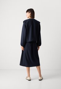 Marineblauwe gestreepte twee-delige outfit met een losvallende top en een rok tot halverwege de knie. De stof lijkt zacht met een licht gegranuleerde afwerking.