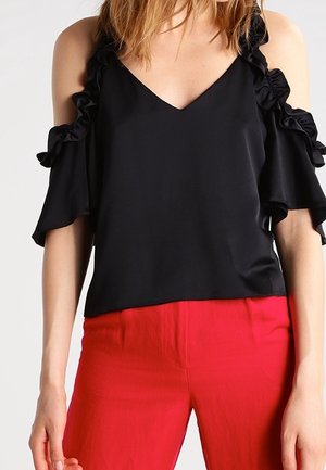 Blusa nera con design a spalle scoperte, con accentuazioni a volant lungo le maniche e scollatura a V. Abbinata a pantaloni rossi, per un look a contrasto.