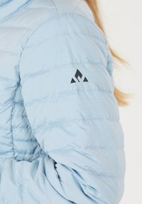 Lysblå pufferjakke med quiltet struktur og elastiske manchetter; har et sort logo på ærmet. Blødt, let materiale.